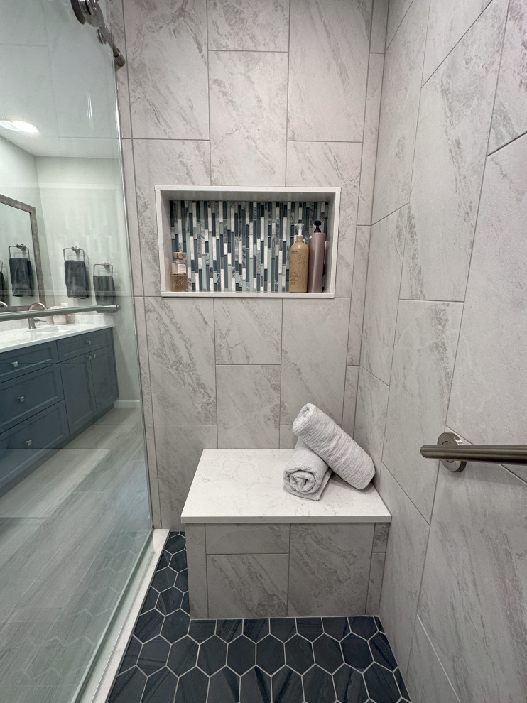 This is an example of a large ensuite bathroom in Detroit with shaker cabinets, blue cabinets, a double shower, a two-piece toilet, grey tiles, porcelain tiles, white walls, porcelain flooring, a submerged sink, engineered stone worktops, grey floors, a sliding door, white worktops, a shower bench, double sinks and a built in vanity unit.