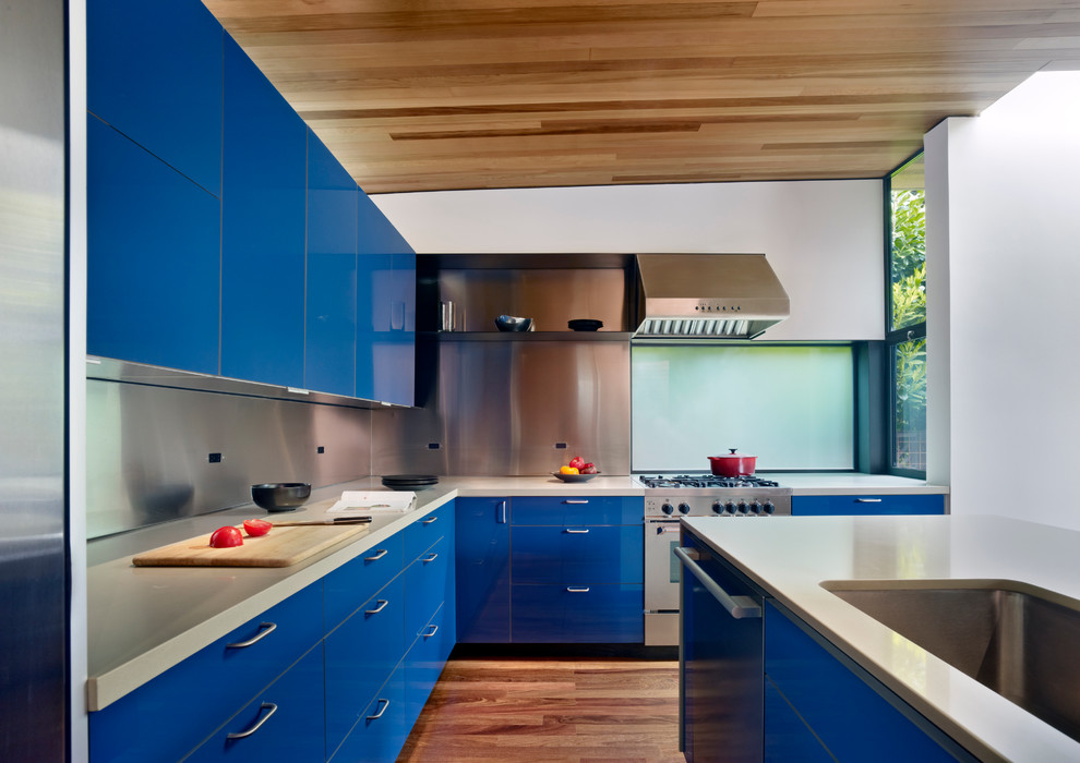 Photo of a mid-sized modern l-shaped eat-in kitchen in San Francisco with flat-panel cabinets, blue cabinets, metallic splashback, an undermount sink, solid surface benchtops, metal splashback, stainless steel appliances, medium hardwood floors and with island.