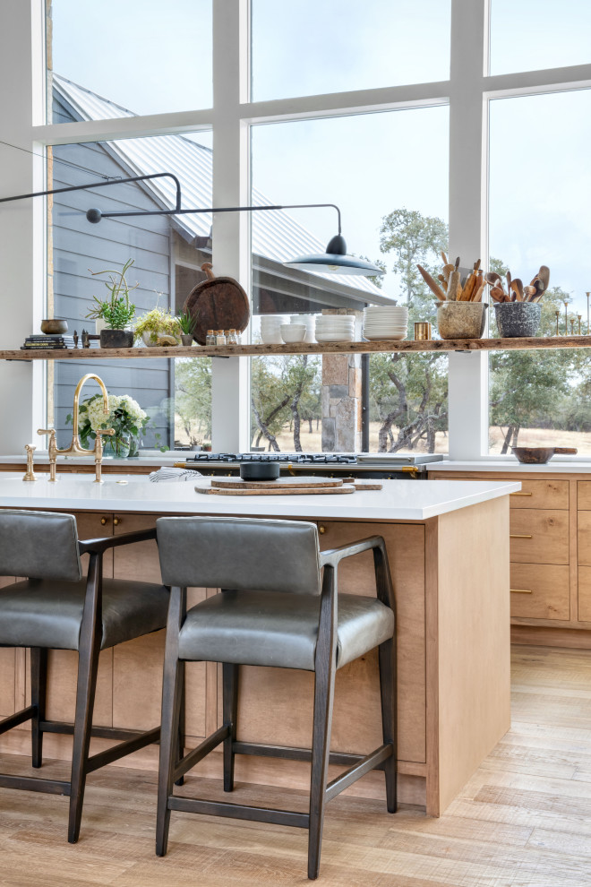 На фото: параллельная кухня-гостиная в стиле кантри с светлыми деревянными фасадами, техникой под мебельный фасад, светлым паркетным полом, островом и белой столешницей
