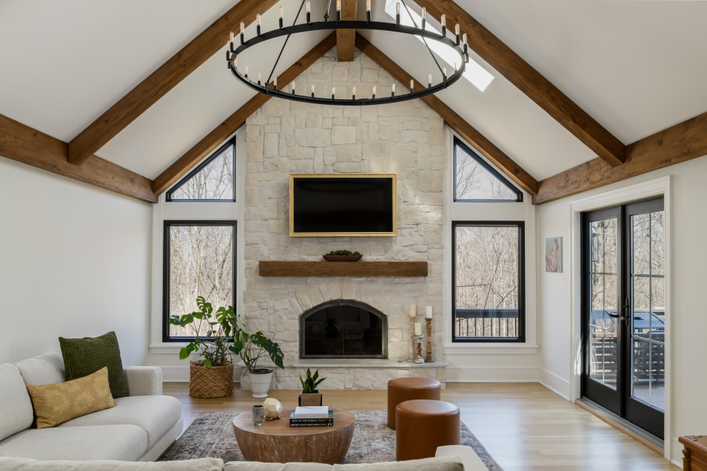 Living room - large transitional open concept light wood floor, brown floor and exposed beam living room idea in New York with white walls, a standard fireplace, a stacked stone fireplace and a wall-mounted tv