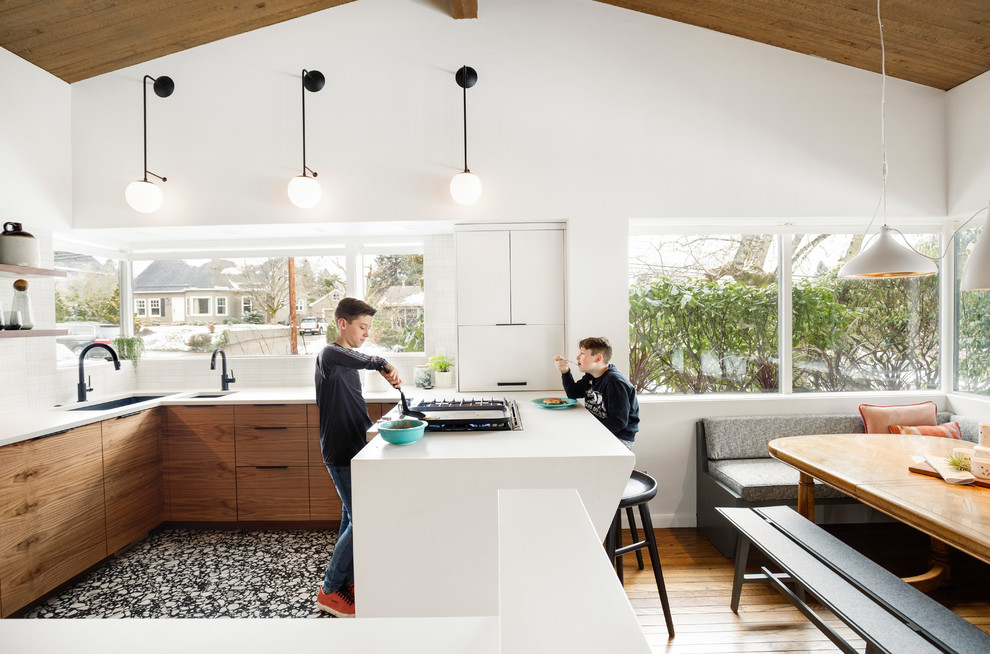 This is an example of a small country u-shaped eat-in kitchen in Portland with an undermount sink, flat-panel cabinets, dark wood cabinets, quartz benchtops, white splashback, ceramic splashback, panelled appliances, terrazzo floors, black floor and white benchtop.
