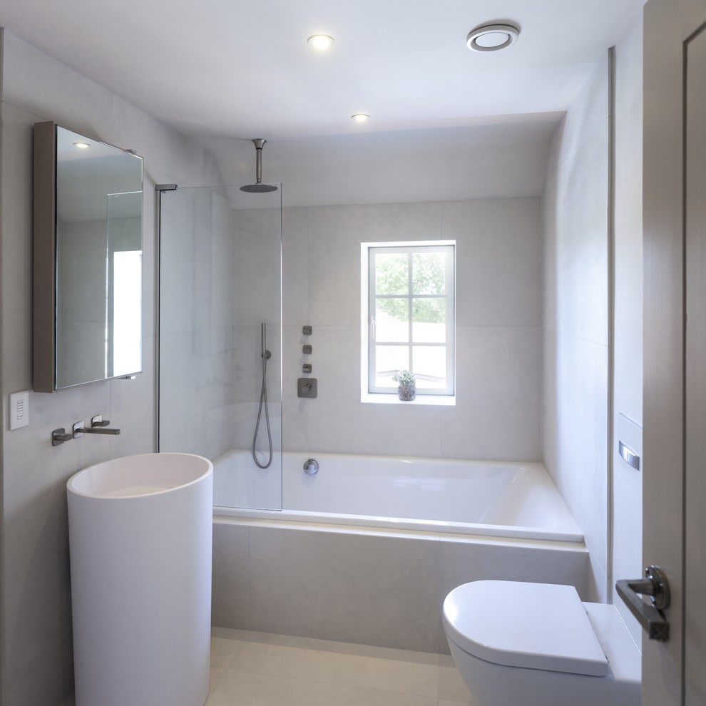 Small contemporary master bathroom in West Midlands with glass-front cabinets, light wood cabinets, a drop-in tub, a shower/bathtub combo, a wall-mount toilet, white tile, white walls and porcelain floors.