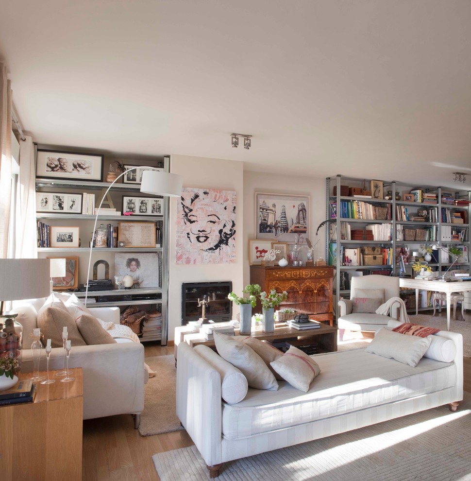 Photo of a large eclectic open concept living room in Madrid with a library, medium hardwood floors, a standard fireplace and beige walls.