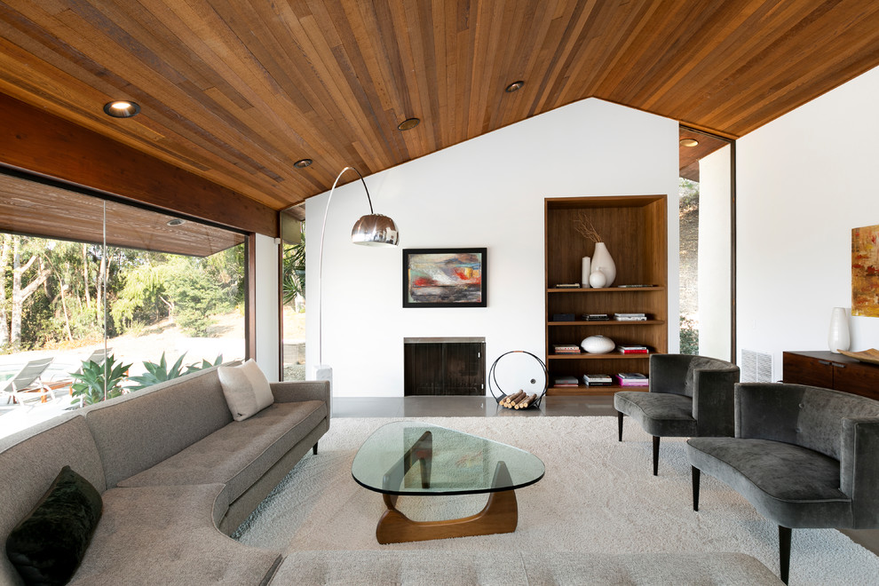 This is an example of a midcentury open concept living room in Los Angeles with a library, white walls, concrete floors, a standard fireplace and no tv.