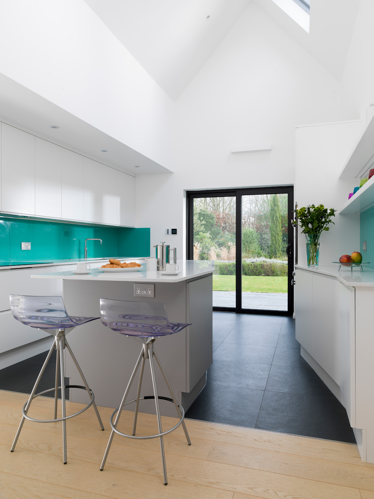Photo of a contemporary kitchen in Other with flat-panel cabinets, white cabinets, green splashback, glass sheet splashback, with island, black floor and white benchtop.