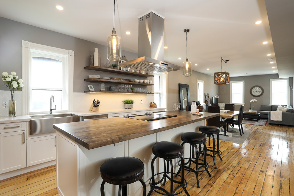 Example of a mid-sized transitional single-wall medium tone wood floor and brown floor eat-in kitchen design with a farmhouse sink, shaker cabinets, white cabinets, white backsplash, stainless steel appliances, an island and white countertops