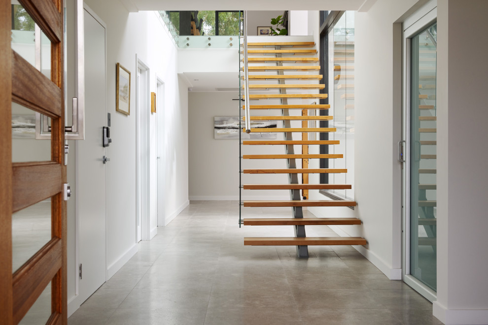 Design ideas for a mid-sized modern wood entry hall in Perth with open risers, glass railing, white walls, a single front door, a medium wood front door and grey floor.