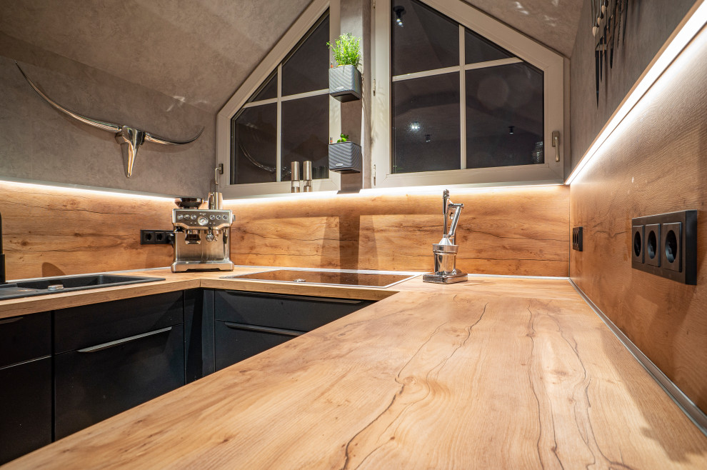 На фото: узкая кухня в современном стиле с черными фасадами, деревянной столешницей, коричневым фартуком, фартуком из дерева и коричневой столешницей