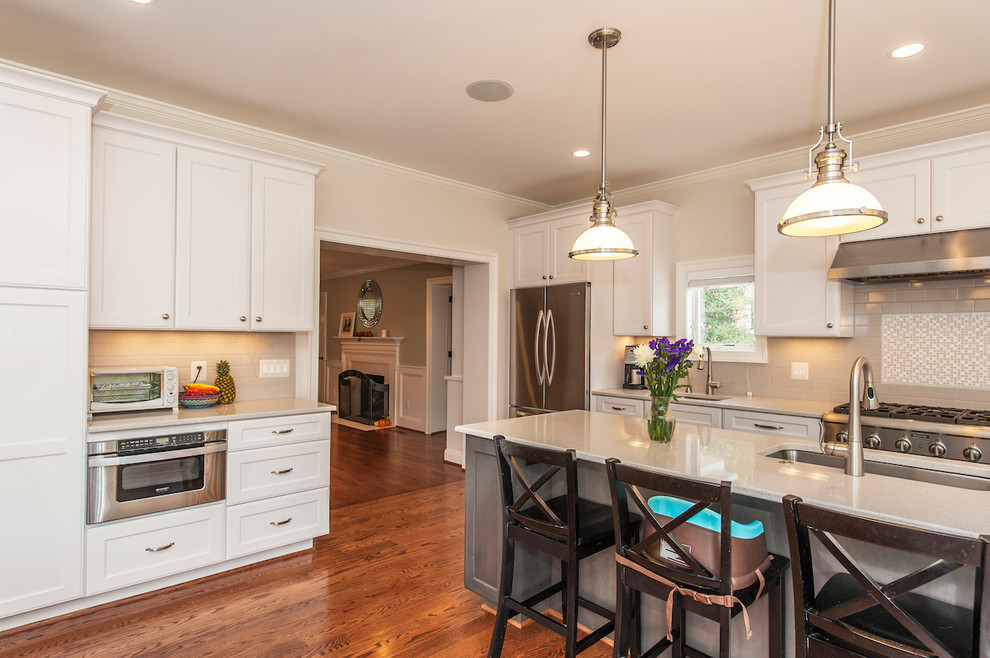 Inspiration for a mid-sized transitional l-shaped medium tone wood floor open concept kitchen remodel in DC Metro with an undermount sink, shaker cabinets, white cabinets, quartz countertops, stone tile backsplash, stainless steel appliances and an island