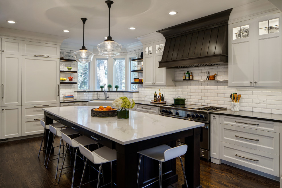 Transitional l-shaped dark wood floor and brown floor kitchen photo in Chicago with a farmhouse sink, white cabinets, white backsplash, subway tile backsplash, an island and black countertops