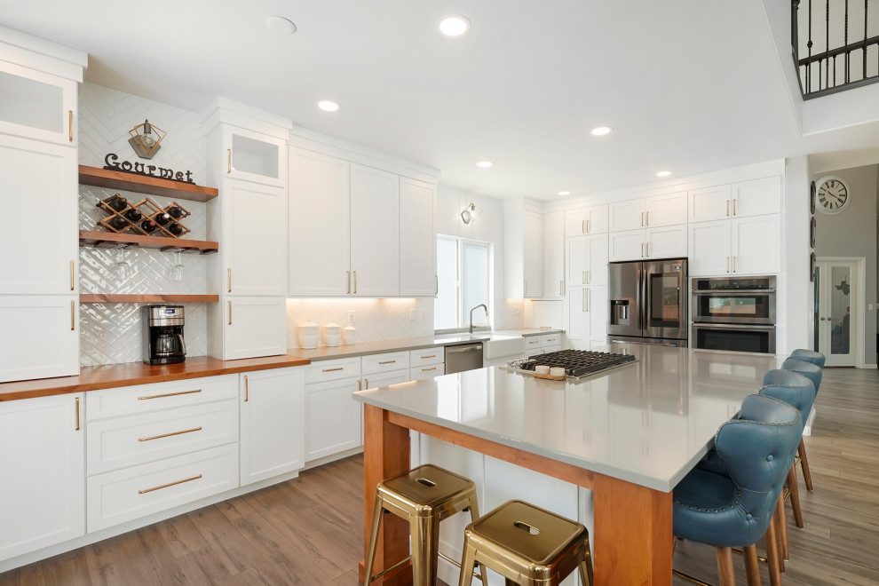 Inspiration for a large transitional l-shaped open concept kitchen remodel in Denver with a farmhouse sink, shaker cabinets, white cabinets, quartz countertops, white backsplash, ceramic backsplash, stainless steel appliances, an island and gray countertops