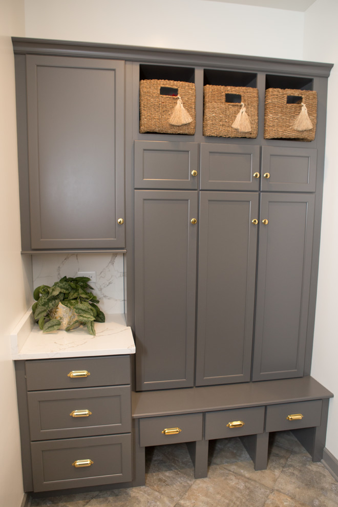 Large transitional u-shaped porcelain tile and gray floor mudroom photo in Chicago with a farmhouse sink, shaker cabinets, gray cabinets, limestone countertops, white backsplash, subway tile backsplash, black appliances, an island, white walls and a gray front door