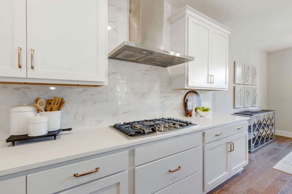 Inspiration for a mid-sized timeless l-shaped medium tone wood floor and brown floor open concept kitchen remodel in Richmond with a farmhouse sink, recessed-panel cabinets, white cabinets, quartzite countertops, white backsplash, ceramic backsplash, stainless steel appliances, an island and gray countertops