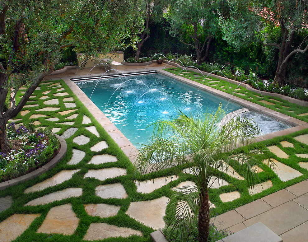 This is an example of a mid-sized mediterranean backyard rectangular lap pool in Los Angeles with natural stone pavers and a water feature.