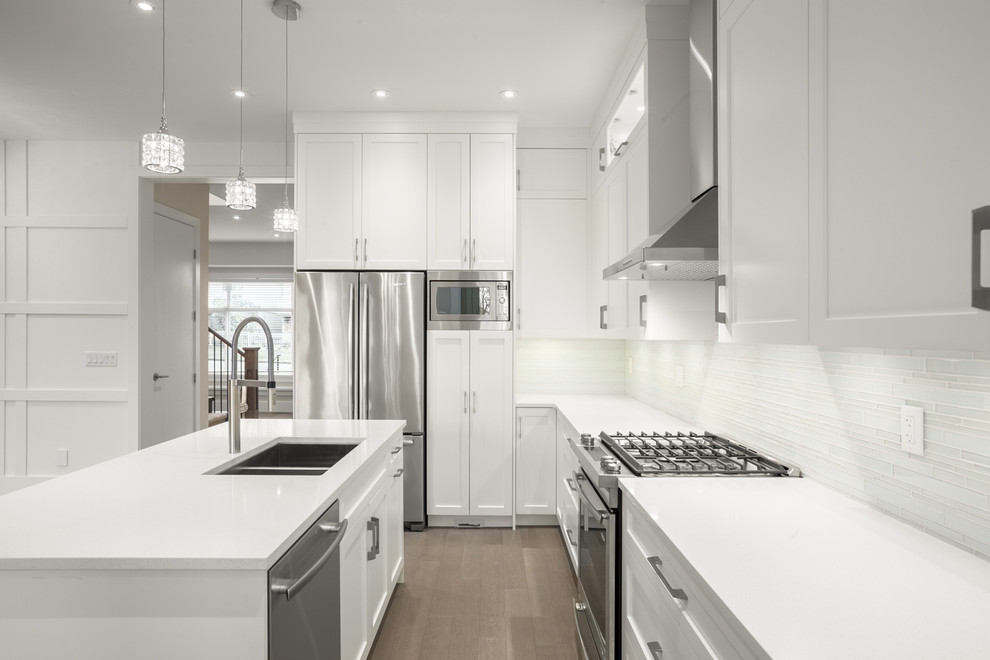 Inspiration for a transitional l-shaped medium tone wood floor eat-in kitchen remodel in Vancouver with an undermount sink, shaker cabinets, white cabinets, quartz countertops, white backsplash, glass tile backsplash, stainless steel appliances and an island