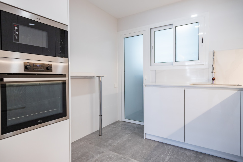 Bild på ett avskilt, mellanstort funkis vit vitt l-kök, med en enkel diskho, släta luckor, vita skåp, vitt stänkskydd, rostfria vitvaror och grått golv