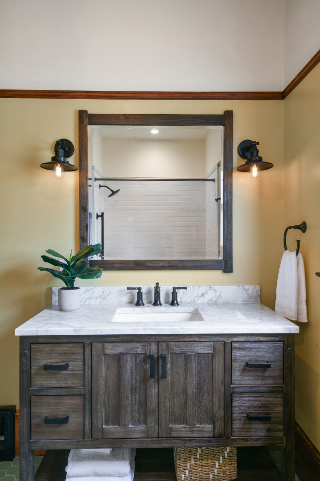 Стильный дизайн: ванная комната среднего размера в стиле кантри с коричневыми фасадами, ванной в нише, душем над ванной, раздельным унитазом, белой плиткой, керамической плиткой, желтыми стенами, полом из керамической плитки, врезной раковиной, мраморной столешницей, зеленым полом, шторкой для ванной, серой столешницей, нишей, тумбой под одну раковину и напольной тумбой - последний тренд