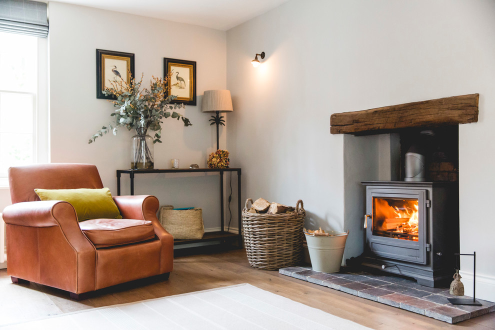 Photo of a country living room in London with white walls, medium hardwood floors, a wood stove and brown floor.