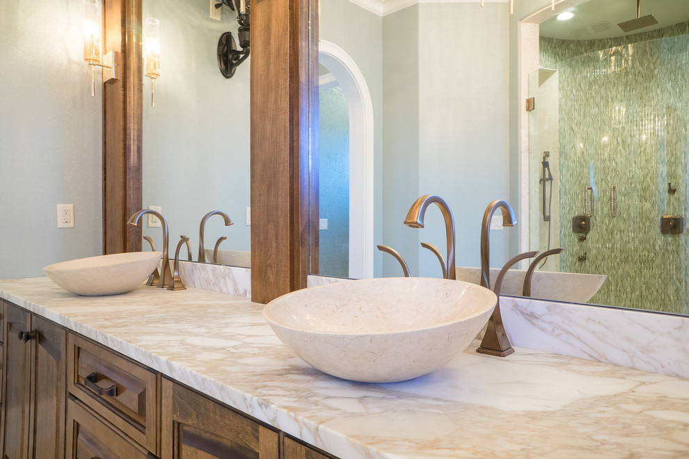 Photo of a large mediterranean master bathroom in Miami with raised-panel cabinets, dark wood cabinets, an alcove shower, blue tile, glass tile, blue walls, limestone floors, a vessel sink, marble benchtops, beige floor and a hinged shower door.