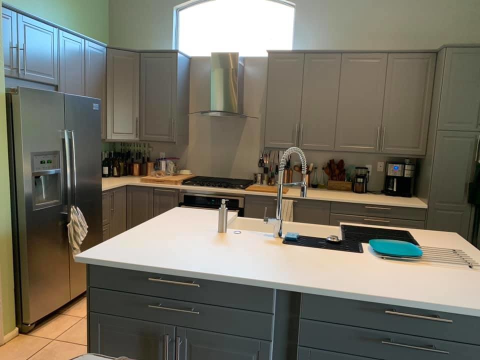 Example of a transitional l-shaped porcelain tile and beige floor open concept kitchen design in Phoenix with a farmhouse sink, raised-panel cabinets, gray cabinets, solid surface countertops, stainless steel appliances, an island and white countertops