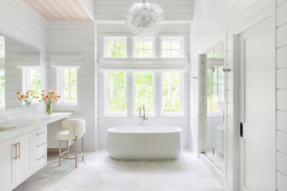 This is an example of an expansive transitional master bathroom in New York with beaded inset cabinets, white cabinets, a freestanding tub, an alcove shower, white walls, marble floors, an integrated sink, marble benchtops, white floor, a hinged shower door, white benchtops, a double vanity, a built-in vanity, vaulted and panelled walls.