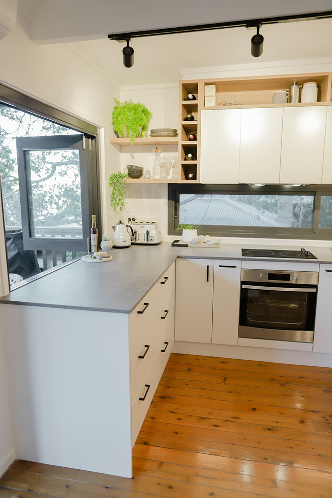 Inspiration for a mid-sized modern l-shaped eat-in kitchen in Central Coast with an undermount sink, flat-panel cabinets, white cabinets, quartz benchtops, grey splashback, window splashback, stainless steel appliances, light hardwood floors, orange floor and grey benchtop.