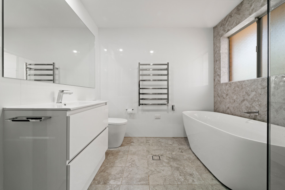 Exemple d'une salle de bain principale bord de mer de taille moyenne avec un placard à porte persienne, des portes de placard blanches, une baignoire indépendante, une douche d'angle, WC à poser, un carrelage gris, des carreaux de porcelaine, un mur gris, un sol en carrelage de céramique, un lavabo intégré, un plan de toilette en stratifié, un sol gris, une cabine de douche à porte battante, un plan de toilette blanc, une niche, meuble simple vasque, meuble-lavabo sur pied et boiseries.