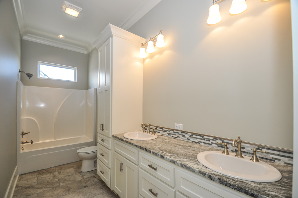 Design ideas for a mid-sized arts and crafts kids bathroom in New Orleans with raised-panel cabinets, white cabinets, an alcove tub, a shower/bathtub combo, a two-piece toilet, gray tile, glass tile, beige walls, ceramic floors, a drop-in sink and granite benchtops.