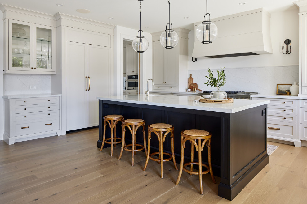 Open concept kitchen - large transitional u-shaped light wood floor open concept kitchen idea in Toronto with a farmhouse sink, recessed-panel cabinets, white cabinets, quartz countertops, white countertops, white backsplash, porcelain backsplash, paneled appliances and an island