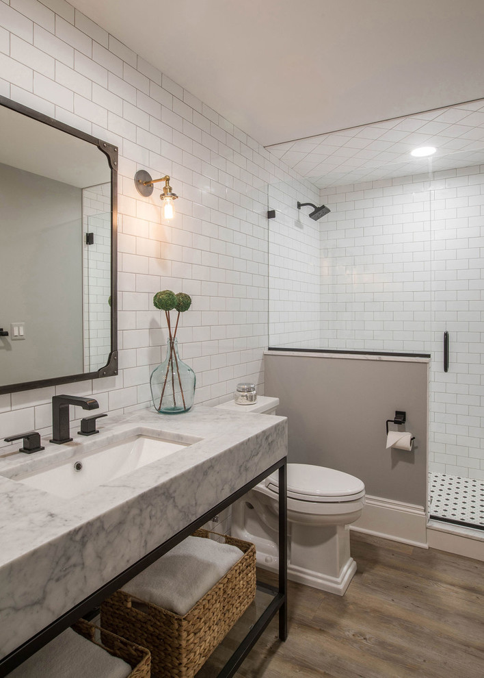 Photo of a mid-sized industrial 3/4 bathroom in Detroit with open cabinets, black cabinets, an alcove shower, a one-piece toilet, white tile, subway tile, white walls, vinyl floors, an undermount sink, marble benchtops, beige floor, a hinged shower door and white benchtops.