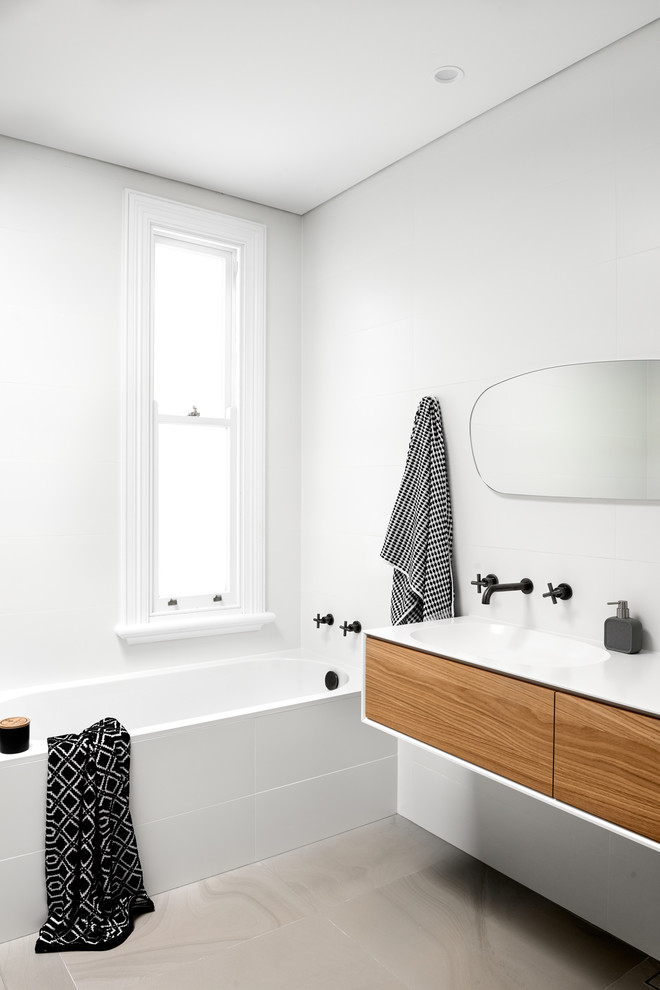 Mid-sized contemporary bathroom in Sydney with flat-panel cabinets, medium wood cabinets, a corner tub, white tile, porcelain tile, white walls, porcelain floors, an integrated sink, solid surface benchtops, grey floor and white benchtops.