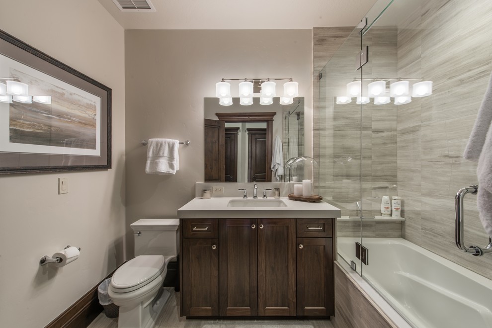 Inspiration for a mid-sized transitional kids bathroom in Salt Lake City with dark wood cabinets, a drop-in tub, a two-piece toilet, gray tile, grey walls, a drop-in sink, solid surface benchtops, grey floor, a hinged shower door, flat-panel cabinets, travertine and travertine floors.