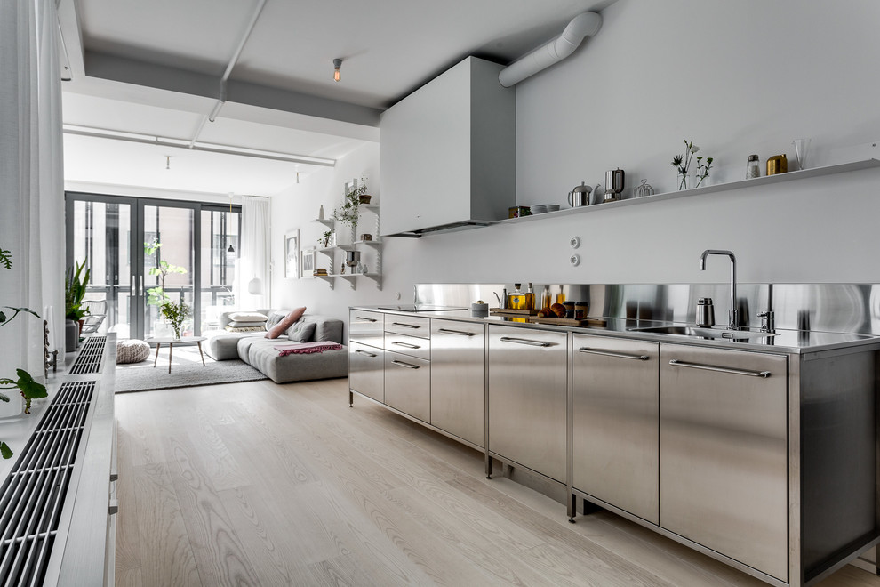 Photo of an industrial kitchen in Stockholm with stainless steel benchtops, a drop-in sink and light hardwood floors.