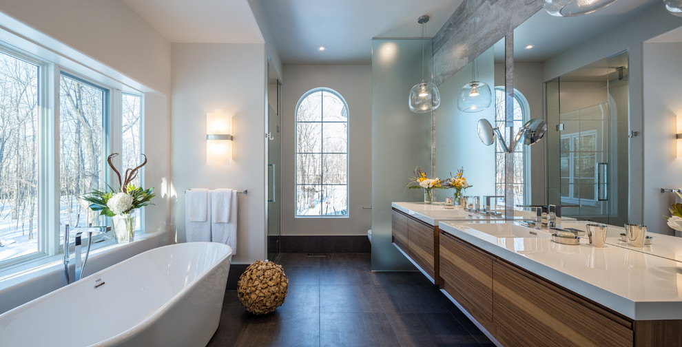 This is an example of a large contemporary master bathroom in Ottawa with flat-panel cabinets, medium wood cabinets, a freestanding tub, an alcove shower, gray tile, porcelain tile, white walls and porcelain floors.