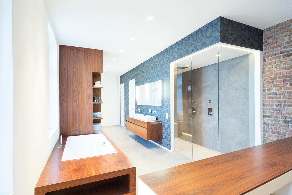 This is an example of an expansive contemporary 3/4 wet room bathroom in Cologne with flat-panel cabinets, medium wood cabinets, brown tile, yellow tile, red tile, stone slab, white walls, concrete floors, a vessel sink, solid surface benchtops, grey floor, a sliding shower screen and a drop-in tub.
