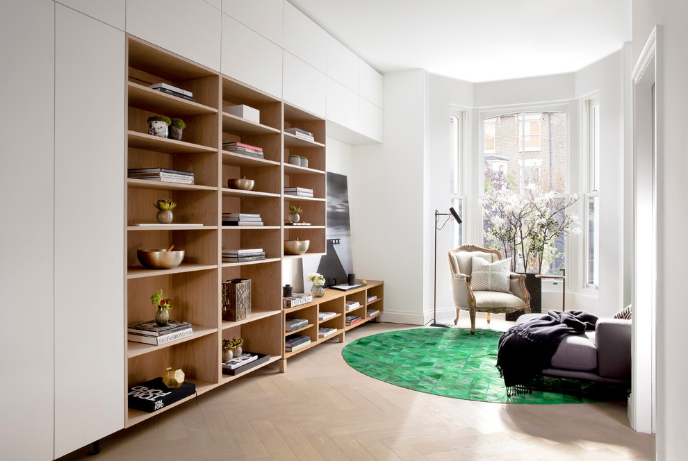 Photo of a mid-sized contemporary open concept family room in London with white walls, light hardwood floors, no tv and a library.