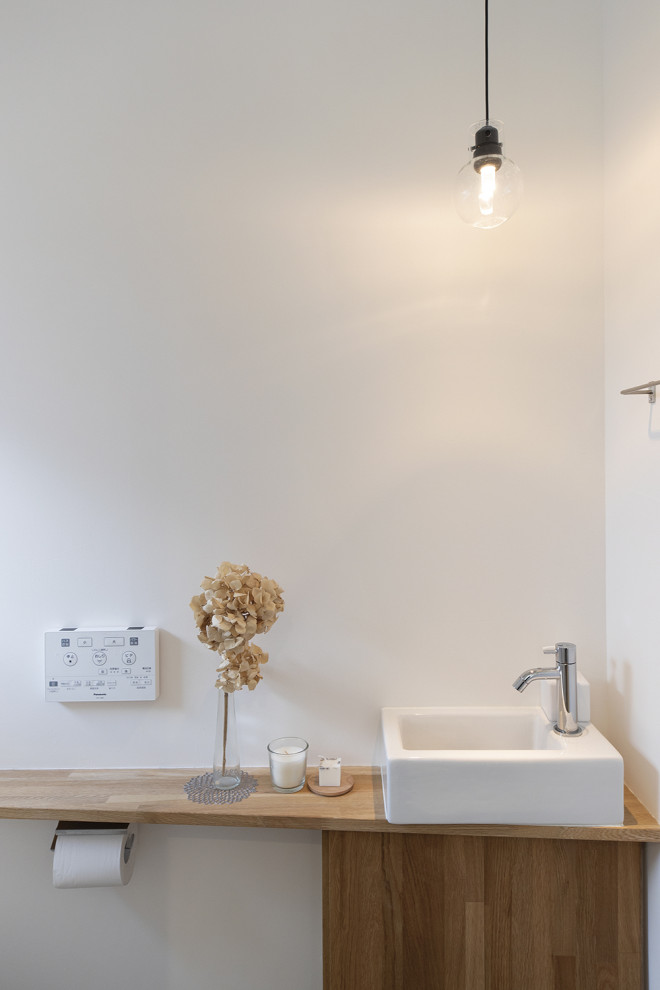 Foto på ett skandinaviskt brun toalett, med släta luckor, skåp i mellenmörkt trä, vita väggar, ett fristående handfat och träbänkskiva