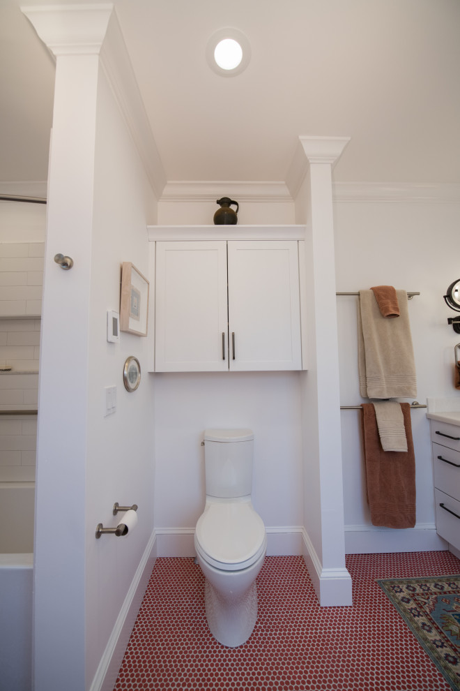 This is an example of a mid-sized eclectic master bathroom in Bridgeport with white cabinets, an alcove tub, a shower/bathtub combo, a two-piece toilet, ceramic floors, an undermount sink, solid surface benchtops, red floor, a shower curtain, white benchtops, a niche, a double vanity and a built-in vanity.