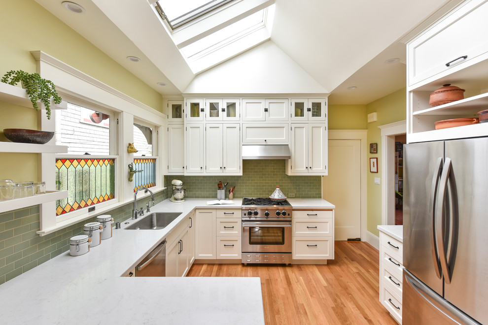 Photo of a transitional kitchen in San Francisco with an undermount sink, recessed-panel cabinets, white cabinets, green splashback, subway tile splashback, stainless steel appliances, medium hardwood floors and a peninsula.