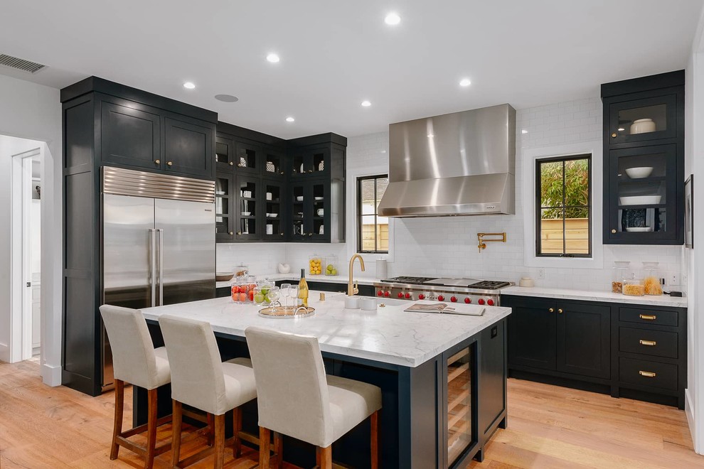Inspiration for a country l-shaped kitchen in Los Angeles with an undermount sink, shaker cabinets, black cabinets, white splashback, stainless steel appliances, medium hardwood floors, with island, brown floor and white benchtop.