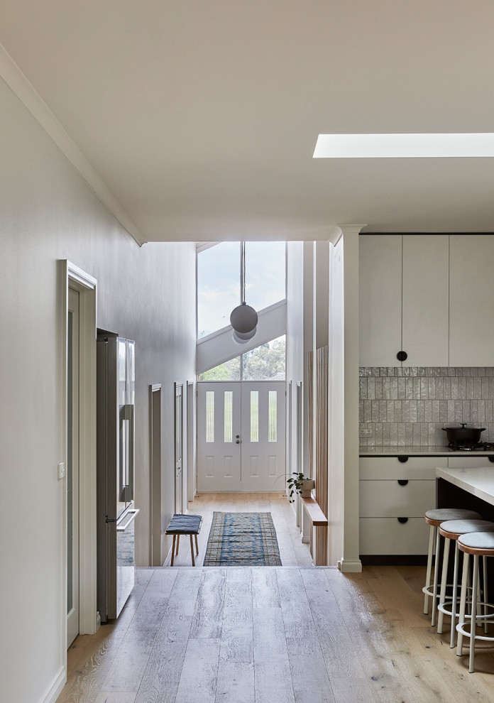 Inspiration for a mid-sized contemporary l-shaped open plan kitchen in Melbourne with a double-bowl sink, white cabinets, quartz benchtops, white splashback, ceramic splashback, stainless steel appliances, light hardwood floors, with island, beige floor and white benchtop.