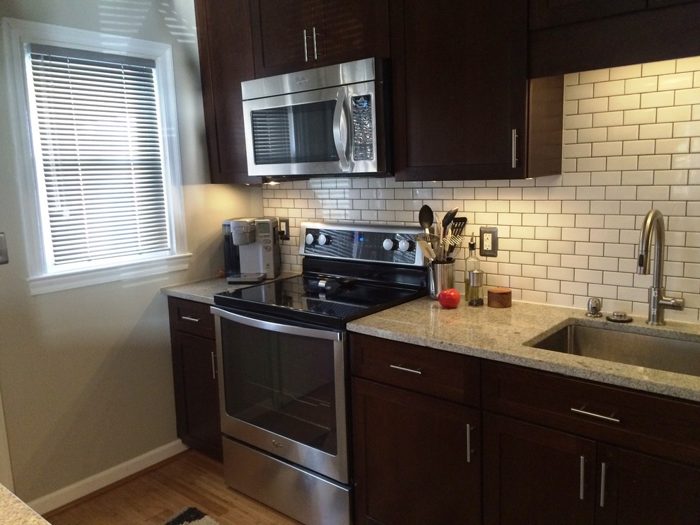 This is an example of a small contemporary single-wall eat-in kitchen in Baltimore with a single-bowl sink, shaker cabinets, dark wood cabinets, granite benchtops, white splashback, subway tile splashback, stainless steel appliances, bamboo floors and a peninsula.