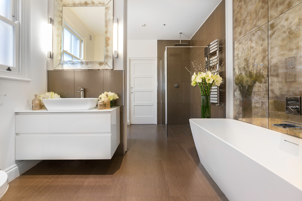 Photo of a contemporary master bathroom in London with flat-panel cabinets, white cabinets, a freestanding tub, an open shower, brown tile, white walls, a vessel sink and an open shower.