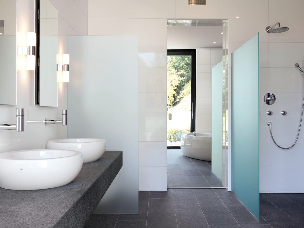 This is an example of an expansive contemporary master bathroom in New York with a vessel sink, a freestanding tub, an open shower, gray tile, white tile, porcelain tile, white walls, porcelain floors, concrete benchtops, an open shower and grey benchtops.