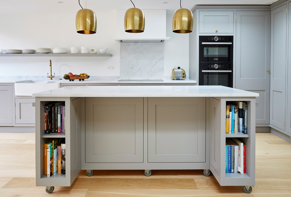 Design ideas for a large contemporary l-shaped eat-in kitchen in London with a farmhouse sink, recessed-panel cabinets, grey cabinets, solid surface benchtops, grey splashback, stainless steel appliances, light hardwood floors and with island.