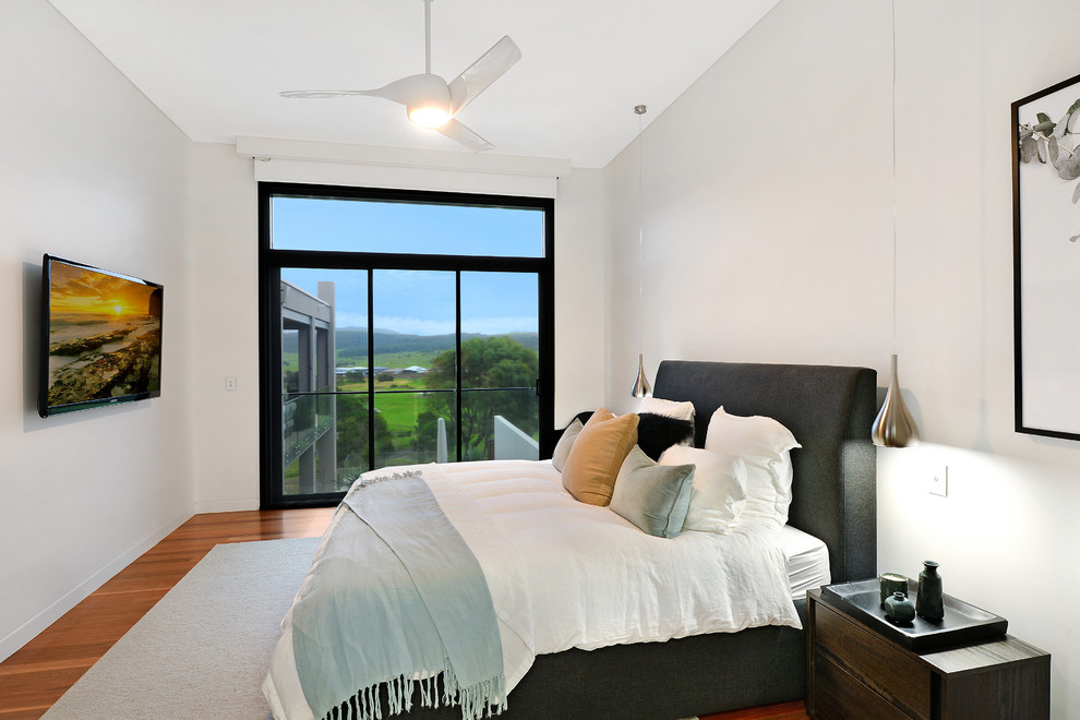 Large transitional bedroom in Wollongong with white walls, medium hardwood floors, no fireplace and brown floor.