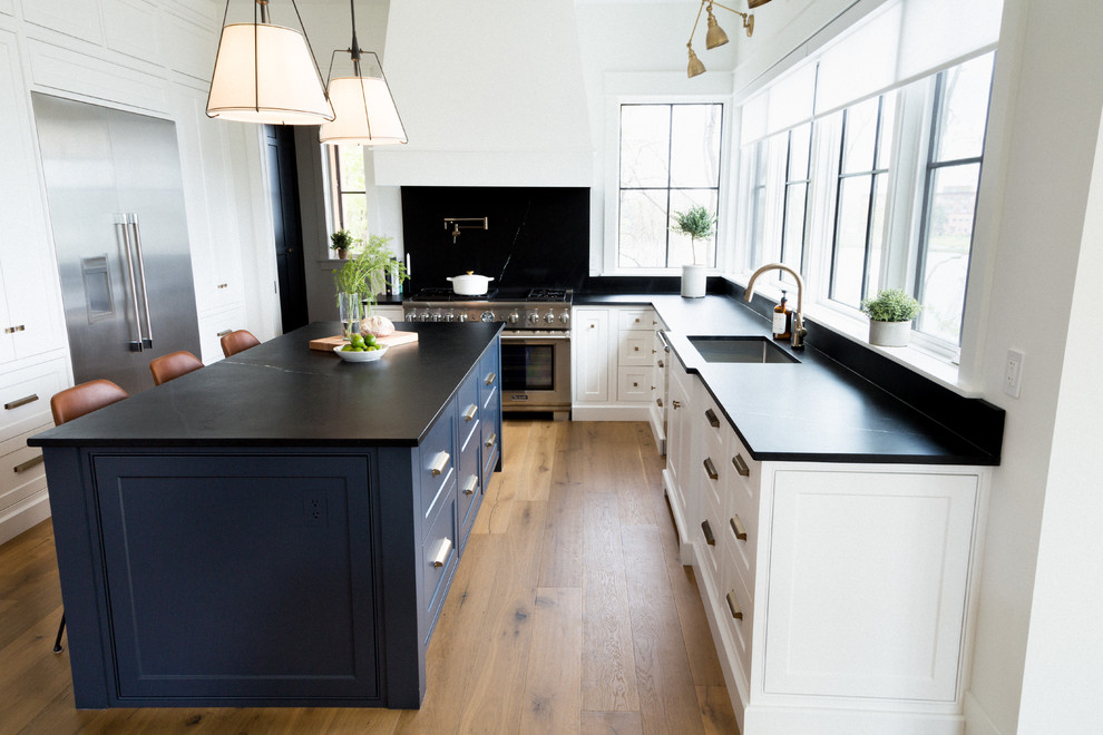 Large transitional u-shaped open plan kitchen in Toronto with an undermount sink, recessed-panel cabinets, white cabinets, limestone benchtops, black splashback, limestone splashback, stainless steel appliances, light hardwood floors, with island, brown floor and black benchtop.