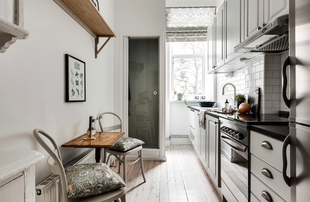 Inspiration for a small scandinavian single-wall eat-in kitchen in Stockholm with white cabinets, light hardwood floors, no island, raised-panel cabinets, white splashback, subway tile splashback and beige floor.