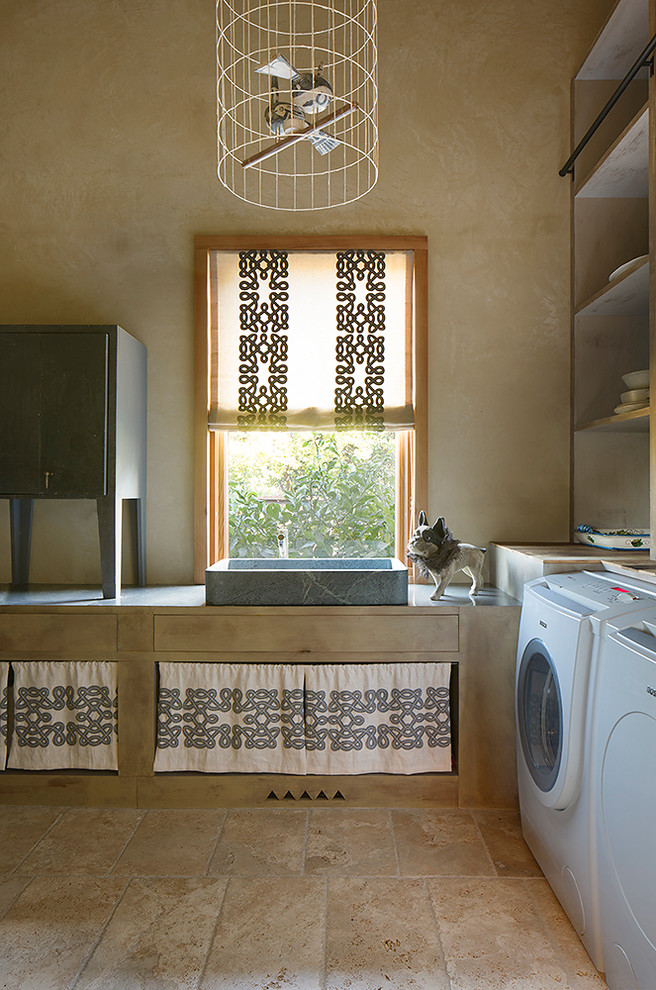 This is an example of a mid-sized country dedicated laundry room in San Francisco with light wood cabinets, beige walls, limestone floors, a single-bowl sink and a side-by-side washer and dryer.