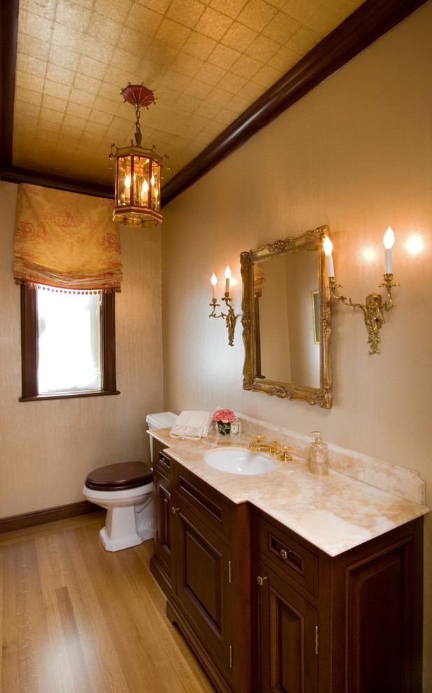 Inspiration for a mid-sized traditional powder room in New York with an undermount sink, beaded inset cabinets, medium wood cabinets, marble benchtops, a one-piece toilet, medium hardwood floors and beige walls.